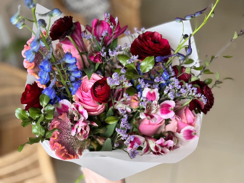 Jewel-toned bouquet of ranunculus, roses and delphinium in white paper